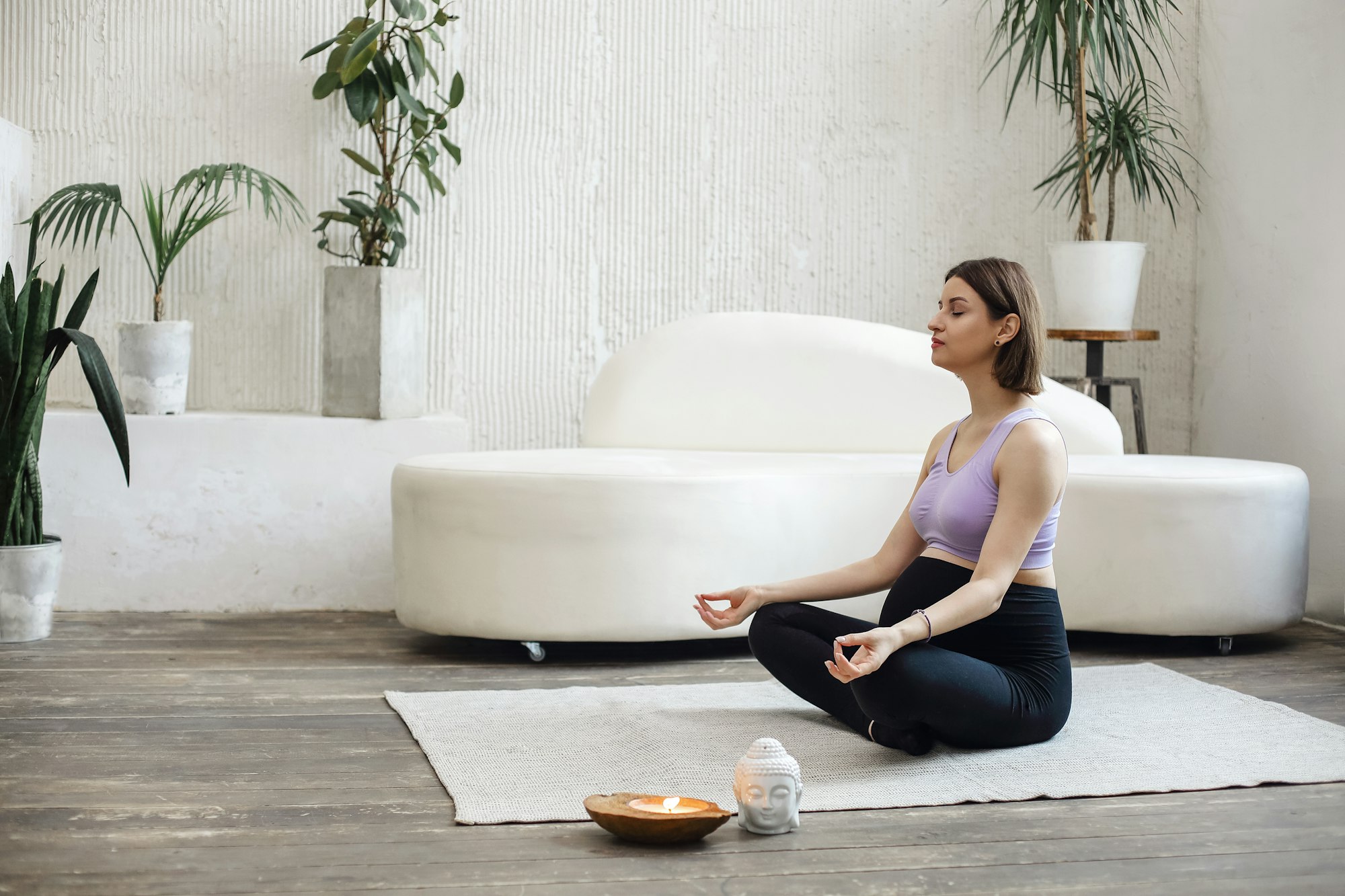 Beautiful pregnant woman sitting in yoga position in spa room, holding coco candle